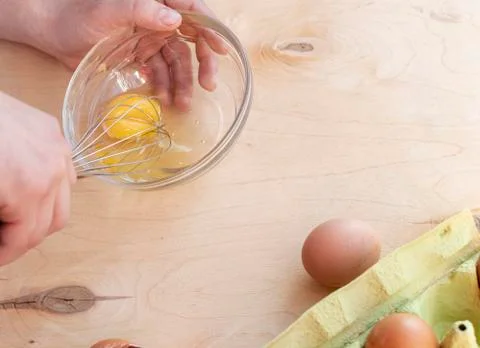 Hands break a raw egg. Stir the protein with the yolk. Glass bowl on a wooden Stock Photos