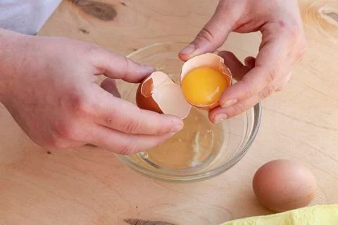 Hands break a raw egg. Stir the protein with the yolk. Glass bowl on a wooden Foto stock