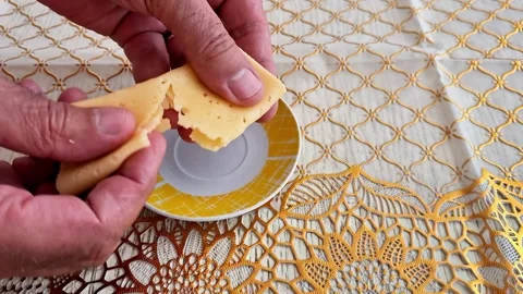 Hands Breaking a Folded Slice of Cheese Over a Decorative Plate on Tablecloth Vidéo 346743595