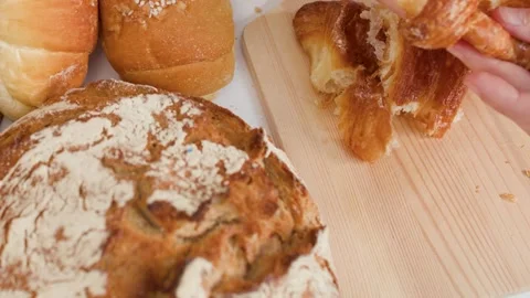 Hands Breaking Fresh Flaky Croissant on Wooden Board Stock Footage 337519563