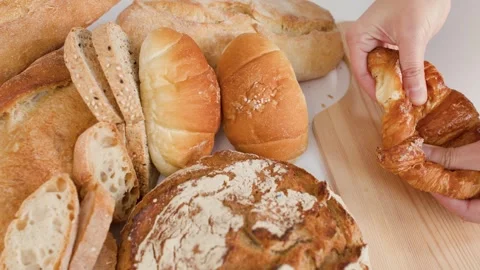 Hands Breaking Fresh Flaky Croissant Over Assorted Bakery Breads Stock Footage 337535544