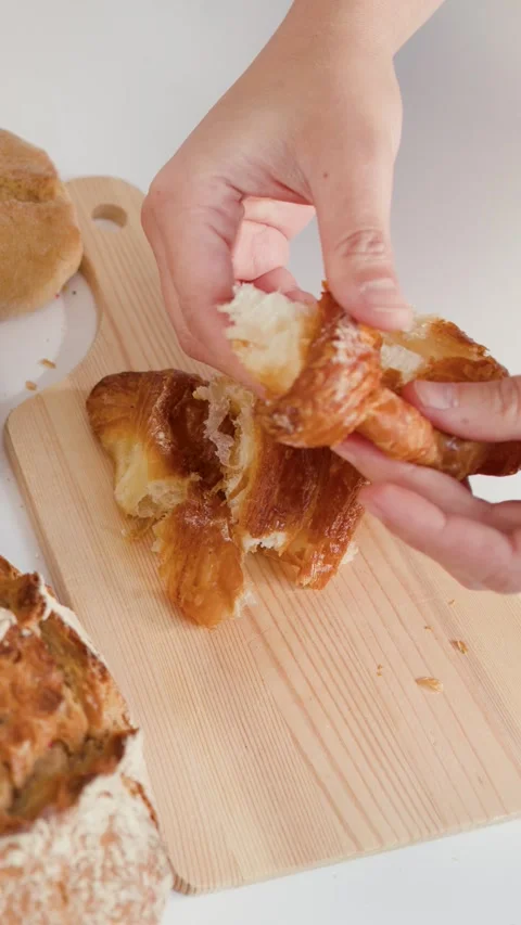 Hands Breaking Fresh Flaky Croissant on Wooden Cutting Board Stock Footage 338051357