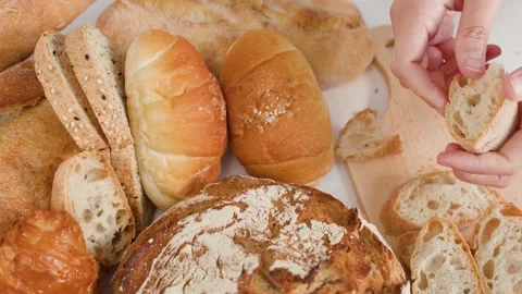Hands Breaking Fresh Sourdough Bread Over Assorted Bakery Selection Stock Footage 337767912