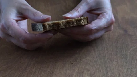 Hands Breaking Slice of Dark Rye Bread into Two Pieces Over Wooden Table Stock Footage 346243367