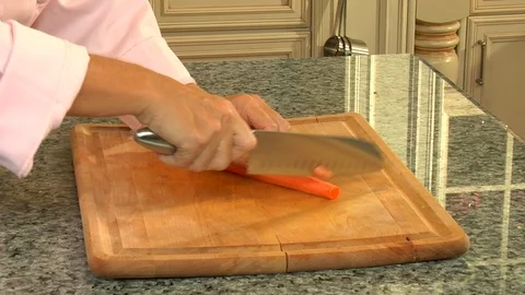 Hands in brightly lit kitchen slicing freshly peeled carrots Video stock 123732625