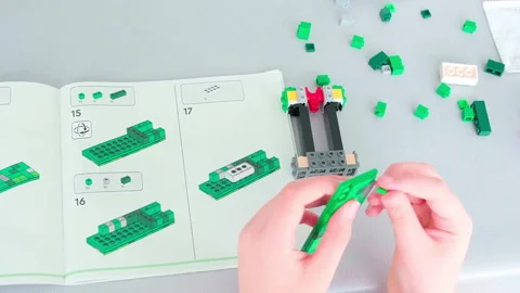 Hands build colorful Lego structure with instruction manual nearby Vidéo 342014481