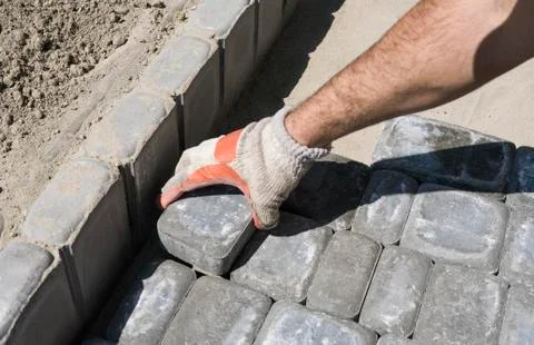Hands of a builder in his orange gloved hands fitting laying new exterior paving Stock Photos