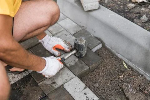 Hands of a builder in his orange gloved hands with a hammer fitting laying new Stock Photos