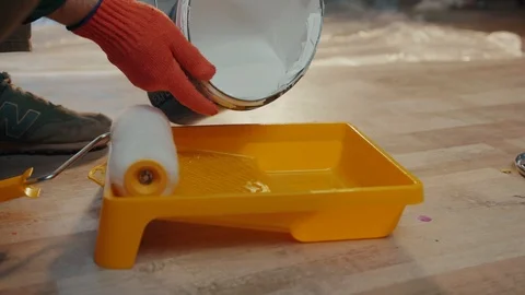 The hands of a builder in orange protective gloves pour out the white paint into Stock Footage 87381364