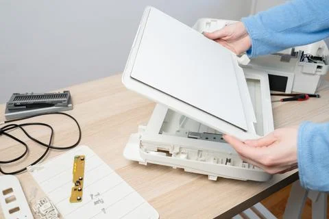 Hands carefully disassembling a flatbed scanner on a wooden desk, showing int Stock Photos
