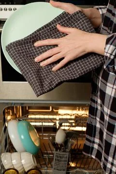 Hands carefully drying a plate while organizing a dishwasher at home Stock Photos