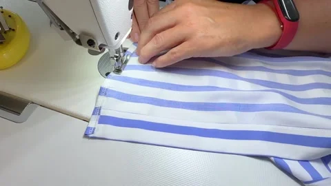 A hands carefully guides a blue and white striped fabric through the needle of a Stock Footage 296074562