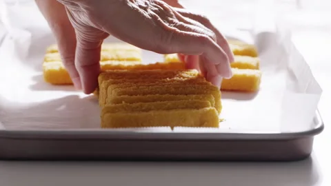 Hands carefully place breaded fish sticks in even rows on a parchment-lined tray Stock Footage 321847722
