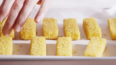 Hands carefully place breaded fish sticks in even rows on a parchment-lined tray Stock Footage 321864289