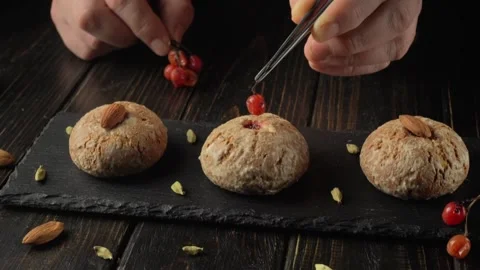 Hands carefully placing red berries viburnum on baked goods arranged on a black Stock Footage 328974556