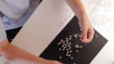 Hands carefully threading glossy beads on fishing line over dark paper back.. Stock Footage 318455530