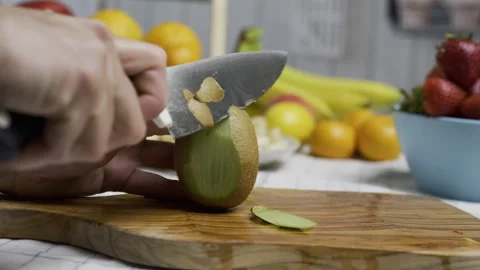 Hands carefully using sharp knife to shave skin off kiwi on cutting board - Stock Footage 341250718