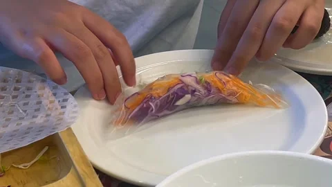 Hands carefully wrap fresh spring roll with colorful vegetables in delicate rice Video stock 301518152