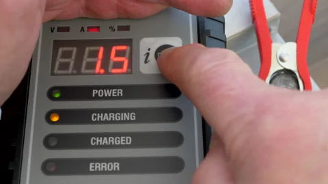 Hands checking readings from a smart charger connected to a vehicle battery. Video stock 151377802