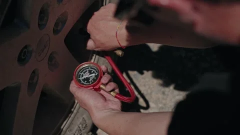 Hands Checking Tyre Pressure with Red Gauge on Off Road Vehicle Wheel Stock Footage 343987000