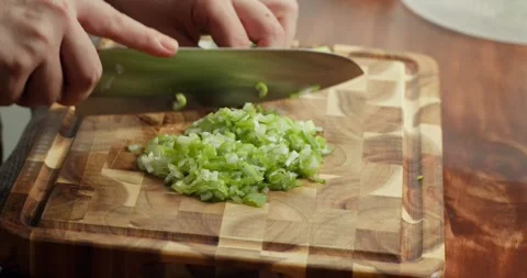 Hands of a chef finely chopping spring onions, parsley, and dill on a wooden Stock Footage 325888709