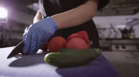 Hands of chef in gloves slicing up a tomato with a knife on cutting board Stock Footage 68851849