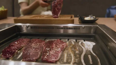 Hands of chef with metallic kitchen tongs turning beef steak on hot grill frying Stock Footage 155351670