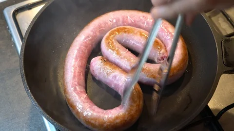 Hands of chef while frying long sausages in pan. Grilled big sausage Stock Footage 113640985
