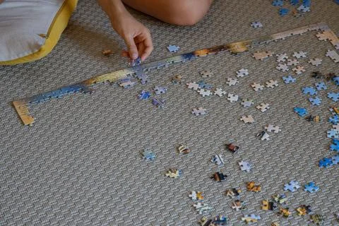 Hands of a child doing on a large jigsaw puzzle on a carpeted floor at home Stock Photos