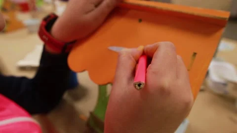 Hands of the child draw with a black pencil on the orange roof of plywood craft Stockbeeldmateriaal 232637853