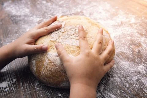 Hands of a child on a loaf of rustic bread Stock Photos