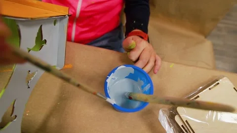 Hands of child pick up gray paint from jar with brush on table and plywood craft Stock Footage 232637847