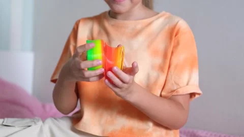 Hands of a child playing orange green slinky, colorful flexible children's toy Stock Footage 255924656