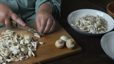 Hands chop fresh champignons with a knife on a cutting board on a wooden ta.. 動画素材 332433907