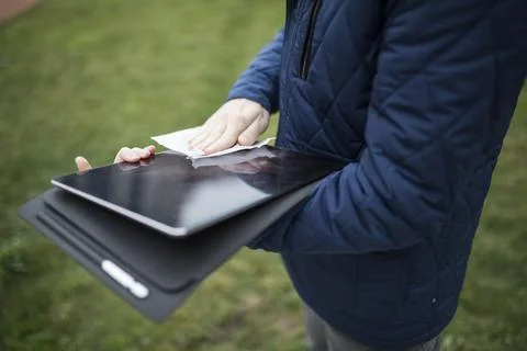 Hands cleaning a tablet touchscreen with a tissue on a green lawn Stock Photos