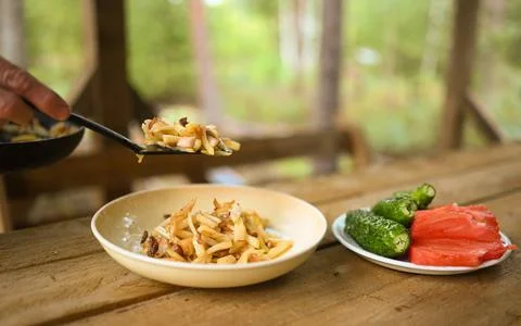 Hands close-up put fried potatoes from frying pan in a plate on wooden table Foto stock