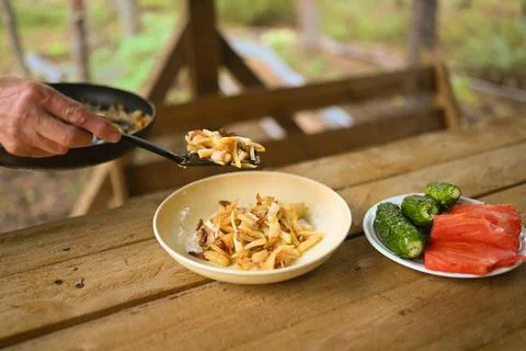 Hands close-up put fried potatoes from frying pan in a plate on wooden table Foto stock