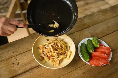 Hands close-up put fried potatoes from frying pan in a plate on wooden table Stock Photos