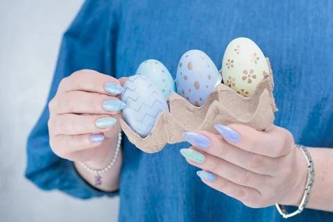 Hands with colored manicure hold Easter eggs. Light yellow, blue and pink color. Stock Photos