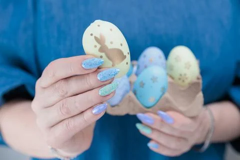 Hands with colored manicure hold Easter eggs. Light yellow, blue and pink color. Stock Photos