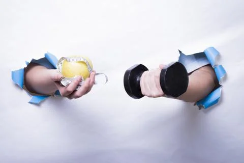 Hands coming out of a white background holding a dumbbell and an apple. Stock Photos