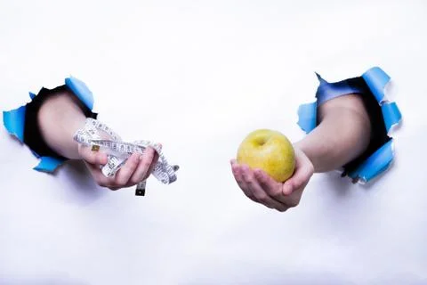 Hands coming out of a white background holding a tape measure and an apple Stock Photos