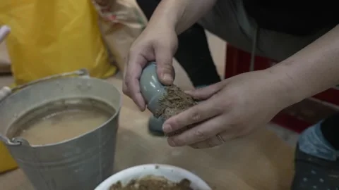 Hands Compacting a Damp Earth Ball Over a Metal Bucket Stock Footage 340901067