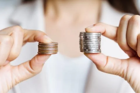 Hands compare two piles of coins of different sizes. Stock Photos