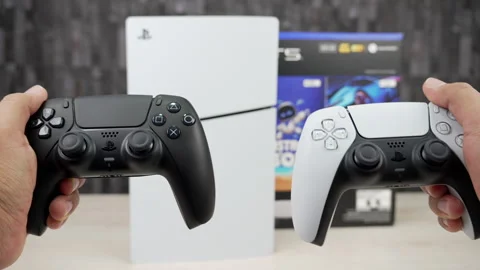 Hands Comparing Black and Gray PS5 DualSense Controllers in Front of Slim Stock Footage 343907700