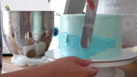 Hands of confectioner leveling with spatula a blue cream on a cake on a rotat Stock Footage 160670275
