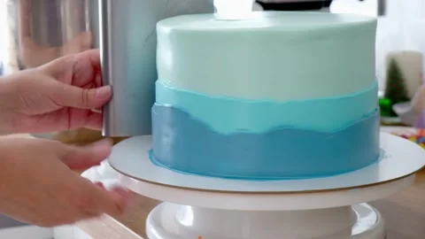 Hands of confectioner leveling with spatula a blue cream on a cake on a rotat Stock Footage 160670276