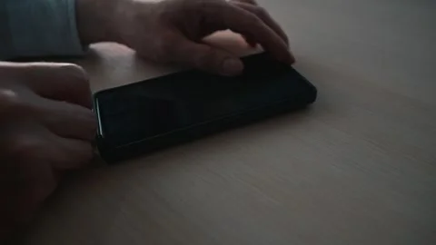 Hands connect a charging cable to a smartphone placed on a wooden surface. Stock Footage 338302656