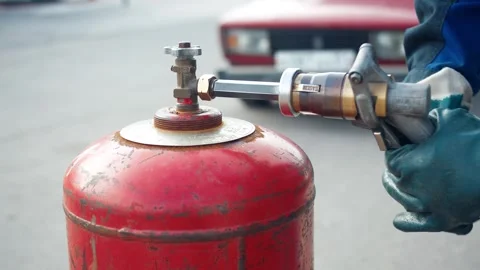 Hands connect a fuel nozzle to a red gas cylinder to fill with liquefied propane Stock Footage 312964212