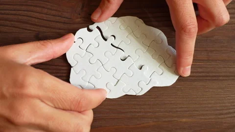 Hands Connecting Puzzle Pieces into Brain Shape on Wooden Surface Stock Footage 295112720